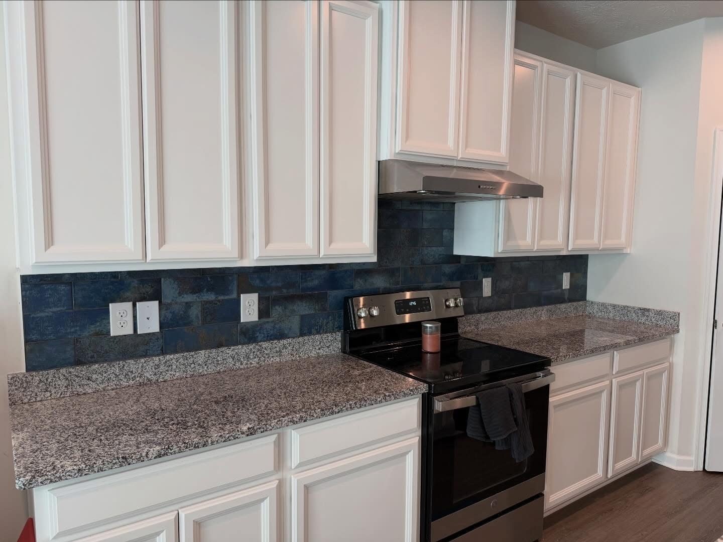 Deep blue glass tile backsplash behind a range with granite counters