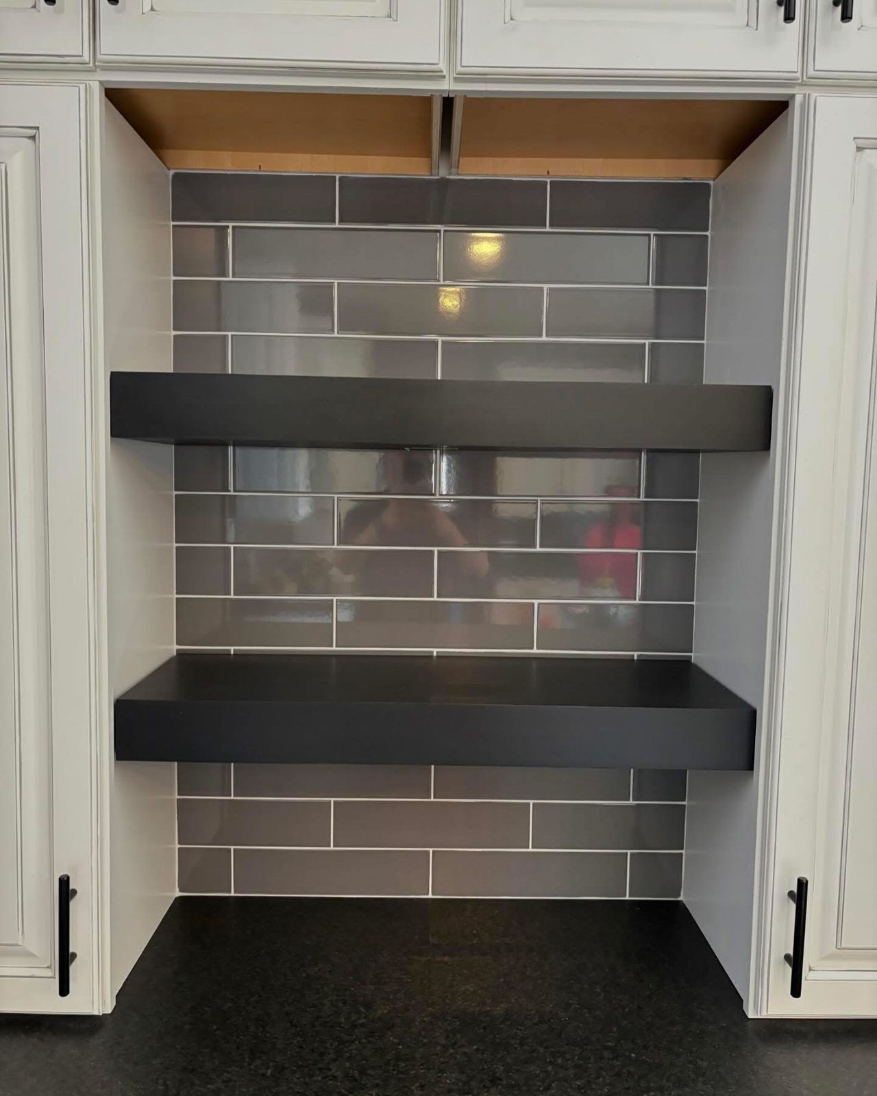 Dark tile backsplash with open shelving between cabinets