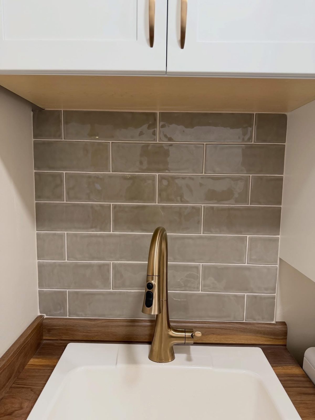 Stone-look tile backsplash above a farmhouse sink with brass faucet