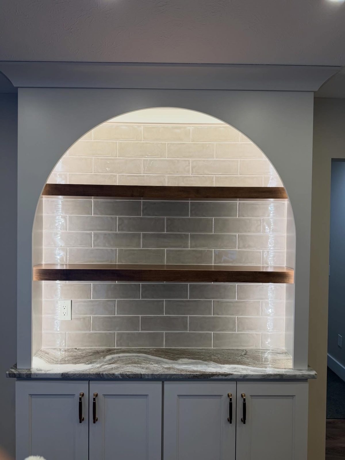 Arched tiled nook with floating wood shelves above a counter